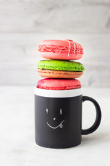 Colourful macarons with happy cup on light background. Romantic concept with copy space. Sweet dessert for coffee break. Concept about love and relationship