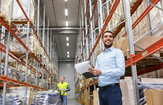 logistic business, shipment and people concept - happy businessman or manager with clipboard and loader at warehouse