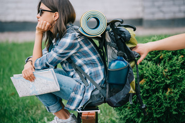 side view of girl traveler holding map and looking away while someone stealing from backpack