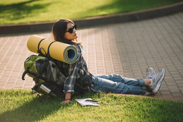 young female traveler with backpack resting on green grass at sunset
