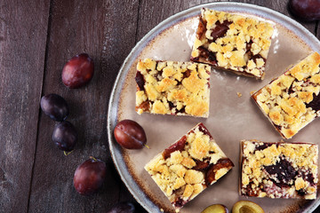 Rustic plum cake on wooden background with plums around.