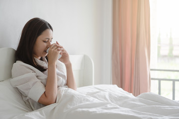Young asian woman drinking morning coffee in bed.