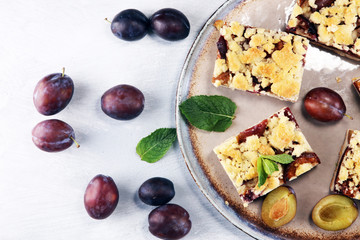 Rustic plum cake on wooden background with plums around.