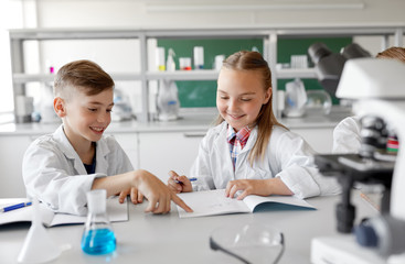 Fototapeta premium education, science and children concept - happy kids with workbooks studying chemistry at school laboratory