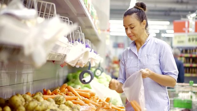 Slender woman buys carrots and put them in a plastic bag in the supermarket