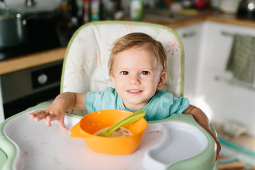 Portrait of adorable baby girl eating at home sitting at baby table .