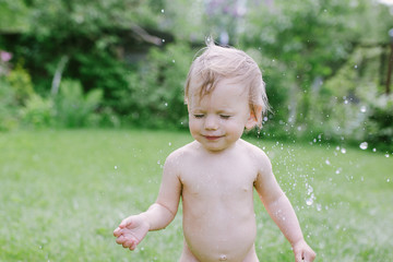 Portrait of adorable baby girl laughing and playing with water in summer garden