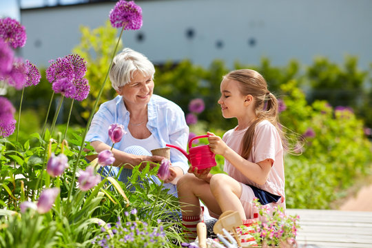 Gardening, Family And People Concept - Happy Grandmother And Granddaughter Planting Flowers At Summer Garden