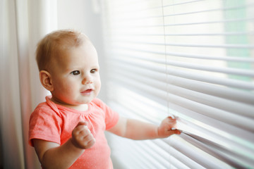 Portrait of cute baby girl touching white louvre shutter .