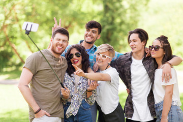 friendship, leisure and technology concept - group of happy smiling friends taking picture by selfie stick at summer park