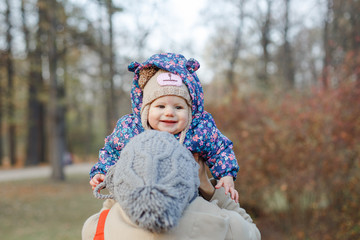 Beautiful young mother holding baby girl in autumn park .