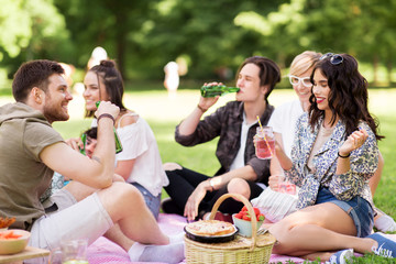 friendship and leisure concept - group of happy friends with non alcoholic drinks and food at picnic in summer park