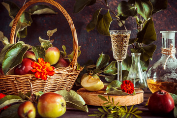 Apple cider in a glass and a decanter and basket with ripe apples on a wooden table in vintage style