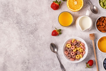 Breakfast with colorful cereal rings, fruit, milk, juice.