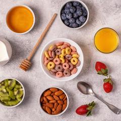 Breakfast with colorful cereal rings, fruit, milk, juice.