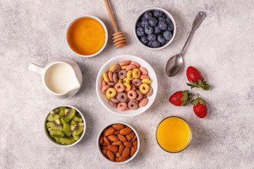 Breakfast with colorful cereal rings, fruit, milk, juice.