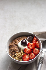 Chocolate oatmeal porridge topped with strawberries, cherries, walnuts and chocolate pieces. The concept of a breakfast. Copy space.