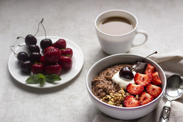 Chocolate oatmeal porridge topped with strawberries, cherries, walnuts and chocolate pieces. The concept of a breakfast. Copy space.