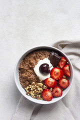 Chocolate oatmeal porridge topped with strawberries, cherries, walnuts and chocolate pieces. The concept of a breakfast. Copy space.