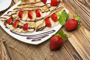 Crepes with Banana, Chocolate and strawberries on a wooden background, pancakes.