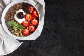 Chocolate oatmeal porridge topped with strawberries, cherries, walnuts and chocolate pieces. The concept of a breakfast. Copy space.