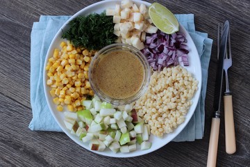 Delicious summer pasta salad on rustic table with corn, apple, red onion, cheese and dill