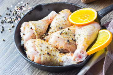 Raw food. Chicken legs (drumsticks) with orange and mustard marinade in cast-iron pan on wooden table background. Cooking content