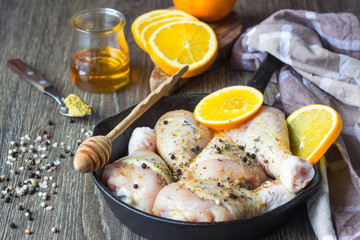 Raw food. Chicken legs (drumsticks) with orange and mustard marinade in cast-iron pan on wooden table background. Cooking content