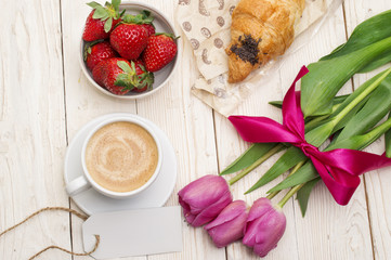Cup of coffee, tulips, croissant and strawberries on wooden background
