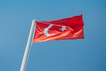 Large flag of Turkey is waving in the wind against the blue sky on a bright sunny day