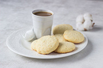 Plate with homemade coconut cookies and a cup of coffee with milk on a light background.
