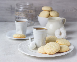 Plate with homemade coconut cookies and a cup of coffee with milk on a light background.