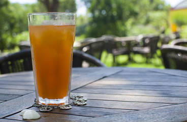 glass with orange juice and ice, accessories bracelet anchor and shells are on a wooden table