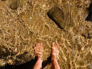 Bare feet wading in shallow stream with sun reflections and ripples.