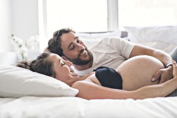 Man with pregnant woman in bed at home having great time - Powered by Adobe