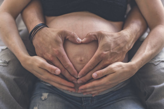 Closeup of heart shape of a couple hands together on the pregnant woman's belly