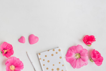 Flat lay desk with pink flowers, notebook and accessories
