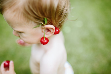 Portrait of cute baby girl with cherries on her ear .