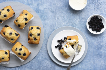 Individual blueberry loaf cakes with a serve on a plate and a bowl of blueberries and a bowl of cream.