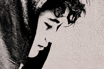 Sad troubled teenager school boy with hood on posing outdoor sitting alone on the street - stock photo made like graffiti stencil painting on white concrete wall
