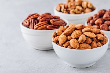 Almonds, pecans, walnuts and hazelnuts in white bowls on grey background. Nuts mix. Healthy food...