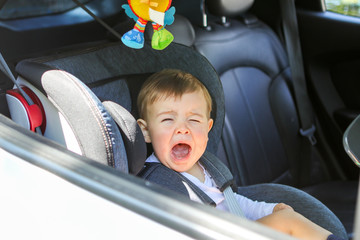 Little baby boy is crying in his car seat not willing to sit in it. Traveling with child and baby safety concept. Little passenger transportation