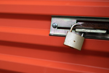 Brass Padlock on Orange Metal Door.