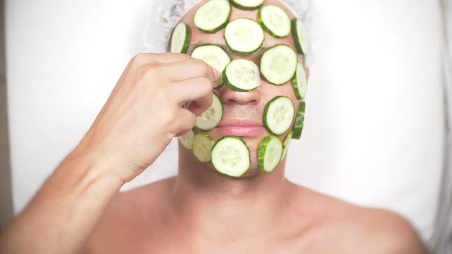 Strange man with face pack. A young man does cosmetic procedures for the face of a house in front of a mirror. 4k, cucumber mask