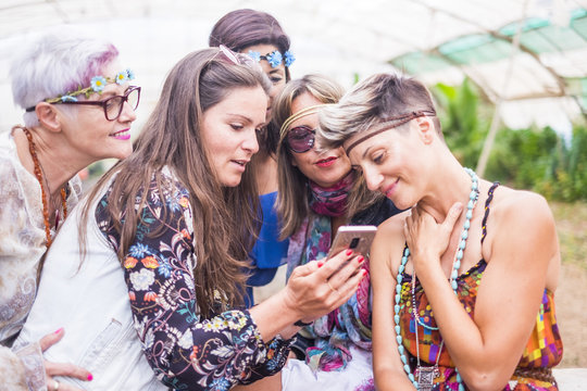 hippy group of caucasian beautiful females looking a smartphone to see a picture or internet results on the web. nice attractive people stay together in happy leisure activity with friendship