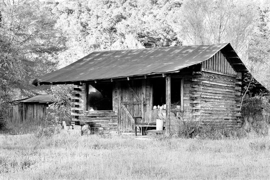 Old, rustic abandoned log cabin in black and white. Little house has square logs, rusty metal roof, and windows with an American Flag. Concepts of Americana, old-fashioned, nostalgia, 