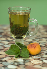 Cup with green tea and green leaves and an apricot