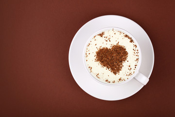 Full white cup of cappuccino coffee on brown