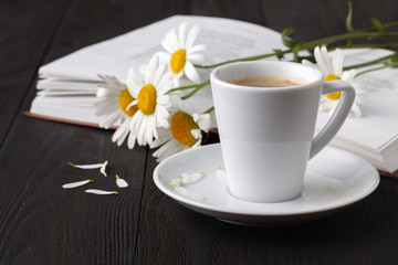 Cup of coffee, chamomile and a book on the wooden table