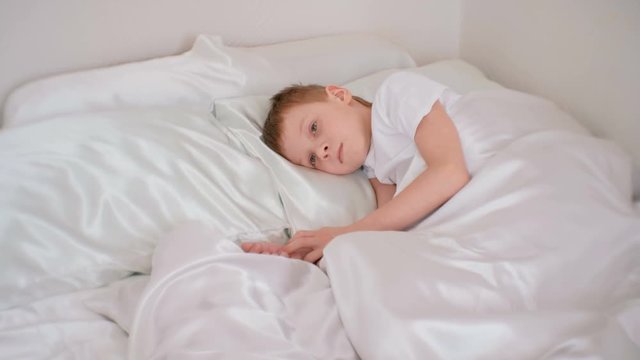 Seven-year-old boy falls asleep lying down in bed.